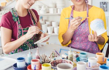 Two women painting own ceramic tableware in DIY workshop with brushes